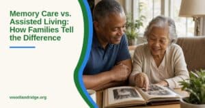 A caregiver and an older woman look through a photo album together at a sunlit table in a calm living space.